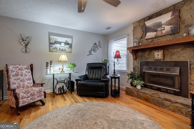 living area featuring hardwood / wood-style flooring, ceiling fan, a fireplace, and a textured ceiling