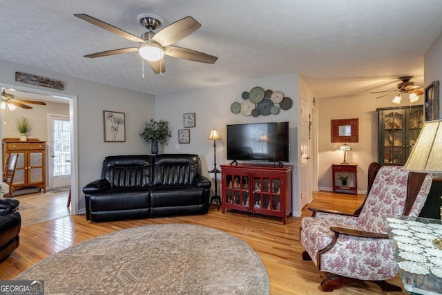 living room featuring ceiling fan, light hardwood / wood-style floors, and a textured ceiling