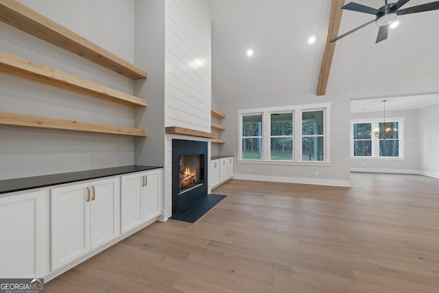 unfurnished living room featuring a large fireplace, ceiling fan with notable chandelier, light hardwood / wood-style flooring, and a towering ceiling