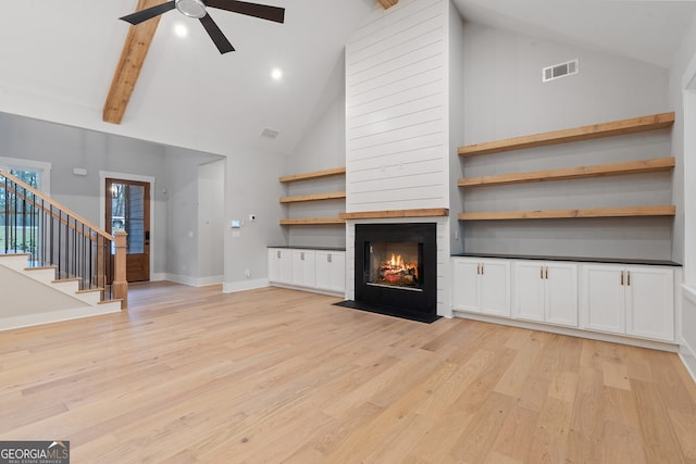 unfurnished living room featuring a fireplace, high vaulted ceiling, light wood-type flooring, ceiling fan, and beam ceiling