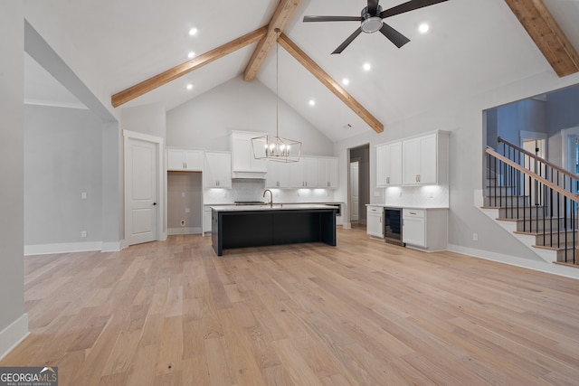 kitchen with white cabinetry, high vaulted ceiling, hanging light fixtures, beverage cooler, and a kitchen island with sink