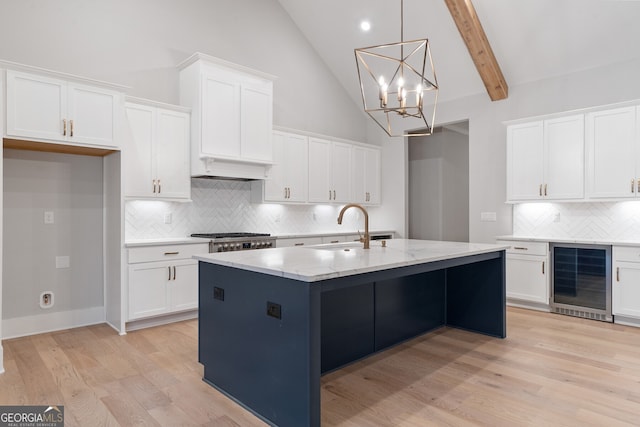 kitchen with white cabinetry, beverage cooler, sink, and a center island with sink