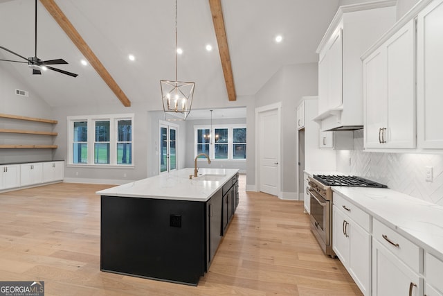 kitchen with sink, a kitchen island with sink, high end range, hanging light fixtures, and backsplash