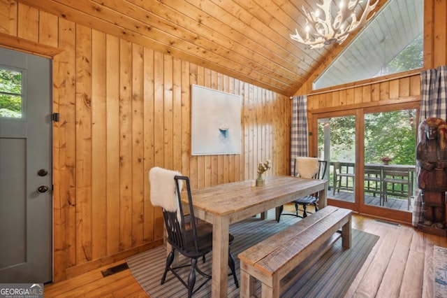 dining area featuring wood walls, wooden ceiling, an inviting chandelier, and light hardwood / wood-style flooring