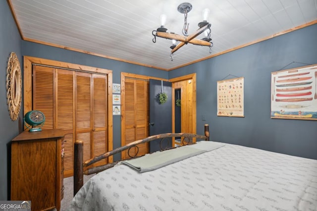 bedroom with crown molding, two closets, and an inviting chandelier