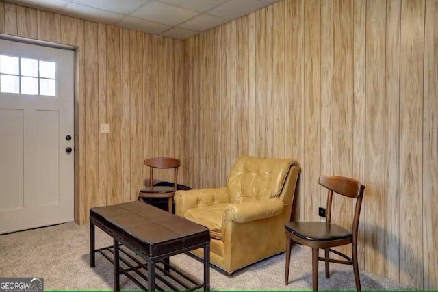 living area with a paneled ceiling, light colored carpet, and wooden walls