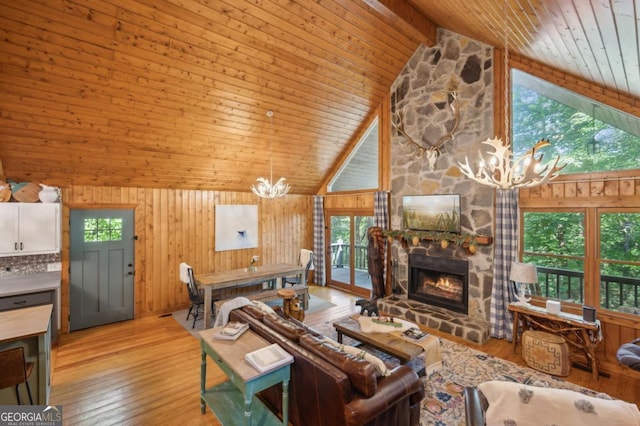 living room with a stone fireplace, a chandelier, light hardwood / wood-style flooring, wooden walls, and beam ceiling