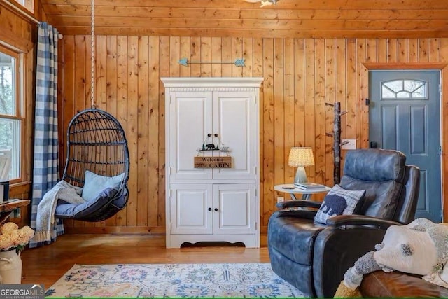 living area with a healthy amount of sunlight, light hardwood / wood-style floors, and wood walls