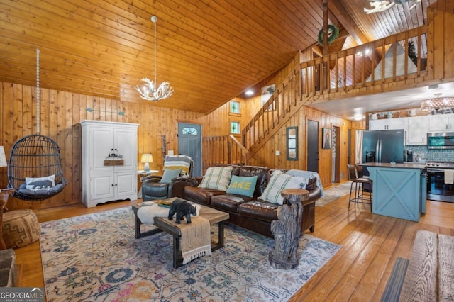 living room with wood ceiling, wooden walls, high vaulted ceiling, a notable chandelier, and light wood-type flooring