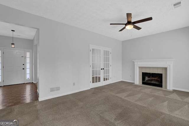 unfurnished living room with a tiled fireplace, ceiling fan, french doors, and a textured ceiling