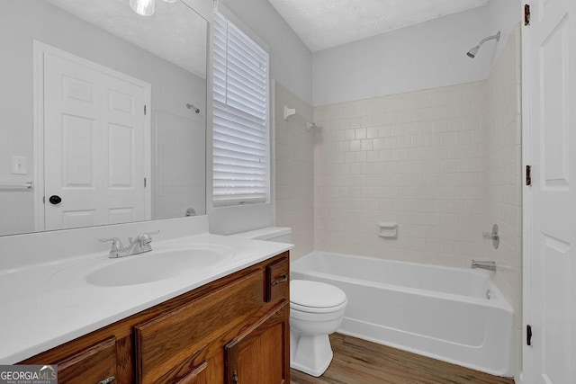 full bathroom featuring tiled shower / bath, hardwood / wood-style floors, vanity, toilet, and a textured ceiling