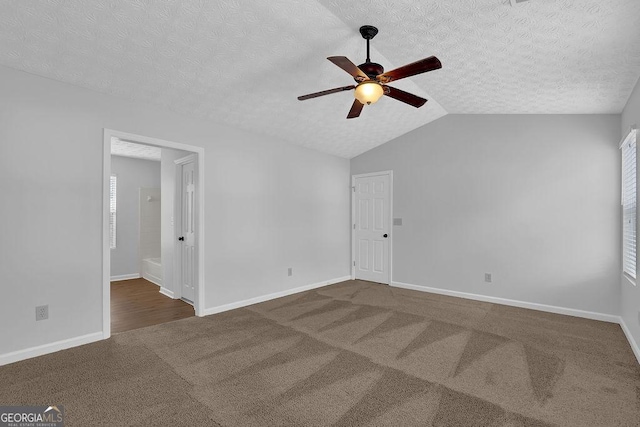 spare room with ceiling fan, vaulted ceiling, a textured ceiling, and dark colored carpet