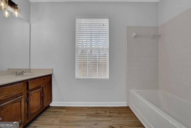 bathroom with hardwood / wood-style flooring, tiled shower / bath, and vanity