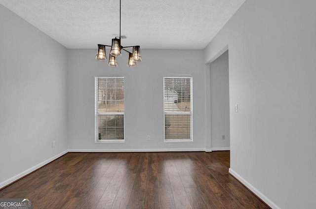 unfurnished dining area featuring dark wood-type flooring, a textured ceiling, and a chandelier