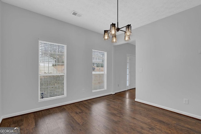 unfurnished dining area with dark wood-type flooring, an inviting chandelier, and a textured ceiling