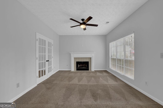 unfurnished living room with a tiled fireplace, light colored carpet, ceiling fan, a textured ceiling, and french doors