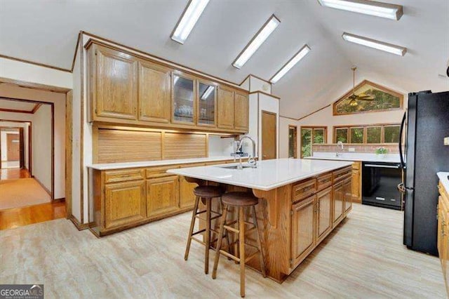 kitchen with sink, a center island with sink, light wood-type flooring, a kitchen breakfast bar, and black appliances