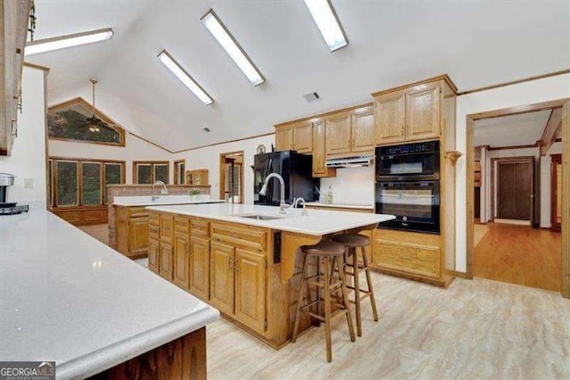 kitchen featuring lofted ceiling, a kitchen bar, light wood-type flooring, an island with sink, and black appliances