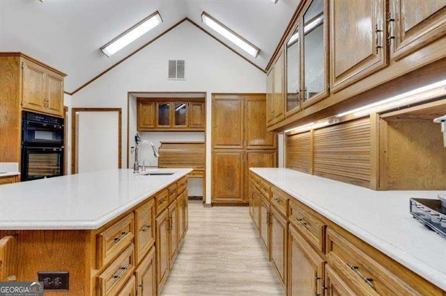 kitchen featuring double oven, lofted ceiling, sink, and an island with sink