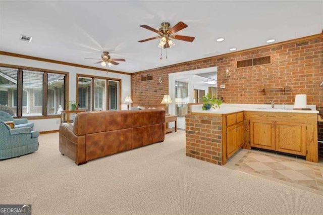 carpeted living room with sink, crown molding, ceiling fan, and brick wall