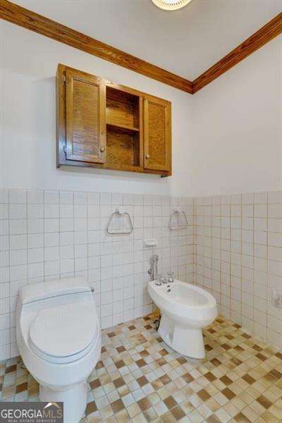 bathroom with a bidet, tile walls, tile patterned floors, and toilet