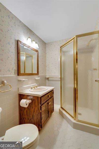 bathroom with tile patterned flooring, tile walls, vanity, a shower with shower door, and toilet