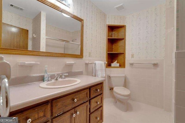 bathroom featuring built in features, a shower, tile walls, vanity, and toilet