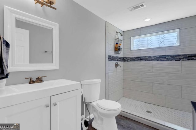 bathroom featuring vanity, wood-type flooring, a tile shower, and toilet