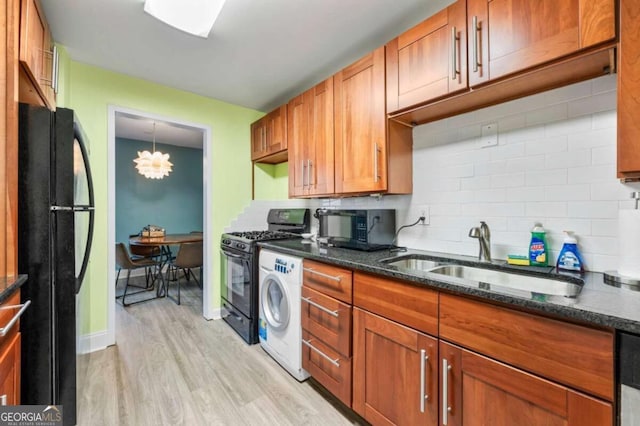 kitchen featuring sink, backsplash, black appliances, light hardwood / wood-style floors, and washer / dryer