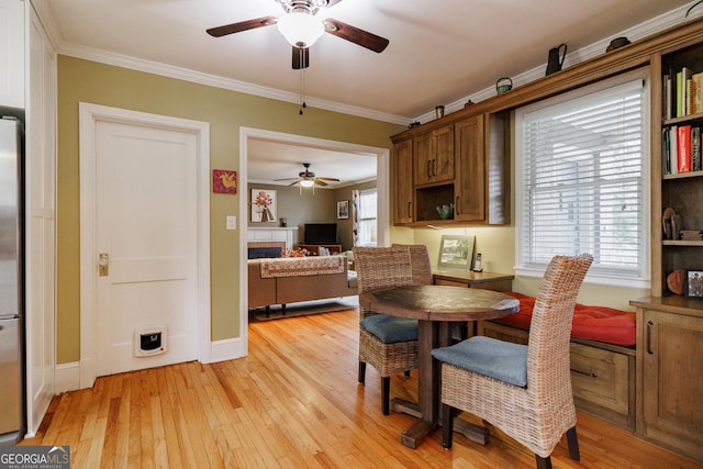 dining area featuring ornamental molding, a tile fireplace, ceiling fan, and light wood-type flooring