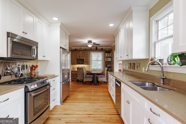 kitchen with appliances with stainless steel finishes, white cabinetry, sink, ceiling fan, and light hardwood / wood-style floors