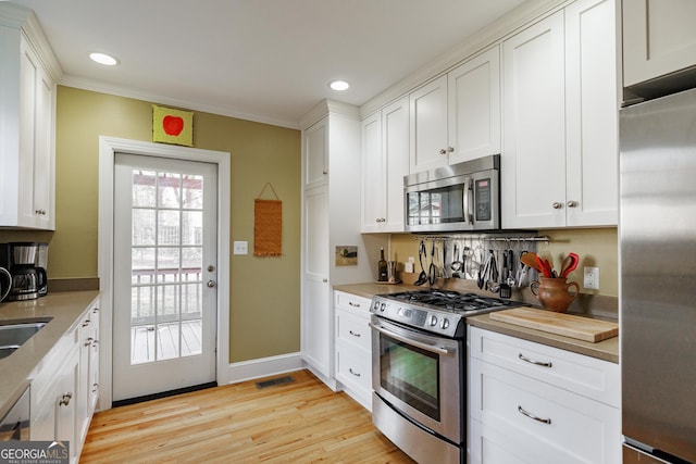 kitchen featuring white cabinetry, stainless steel appliances, crown molding, and light wood-type flooring