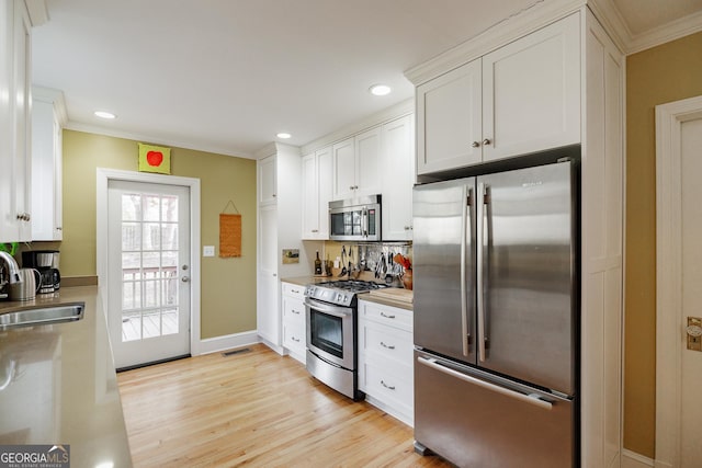 kitchen featuring sink, white cabinets, ornamental molding, light hardwood / wood-style floors, and stainless steel appliances