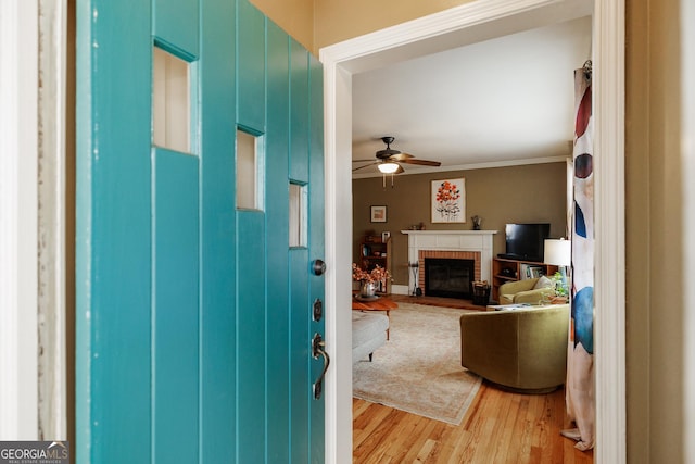 foyer entrance featuring hardwood / wood-style floors, crown molding, a brick fireplace, and ceiling fan