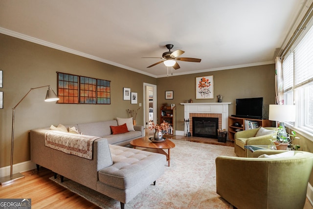 living room featuring crown molding, ceiling fan, a fireplace, and light wood-type flooring