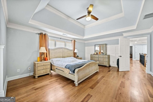 bedroom with ceiling fan, a tray ceiling, and light hardwood / wood-style floors