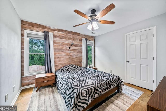 bedroom featuring light hardwood / wood-style flooring, wooden walls, and ceiling fan