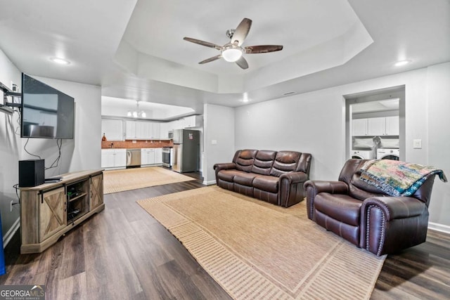 living room with sink, dark hardwood / wood-style flooring, a raised ceiling, washer and clothes dryer, and ceiling fan with notable chandelier