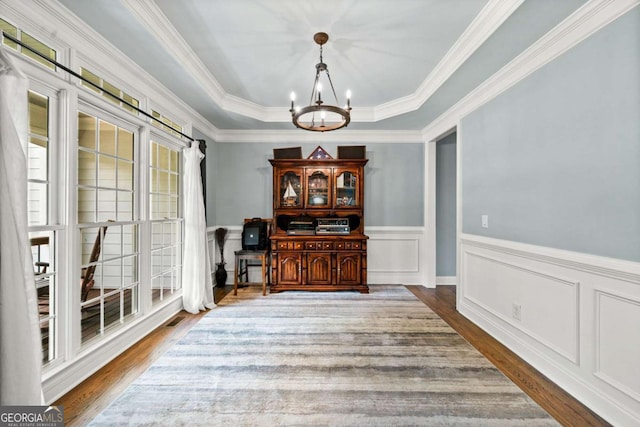 dining space with a raised ceiling, ornamental molding, hardwood / wood-style floors, and a notable chandelier