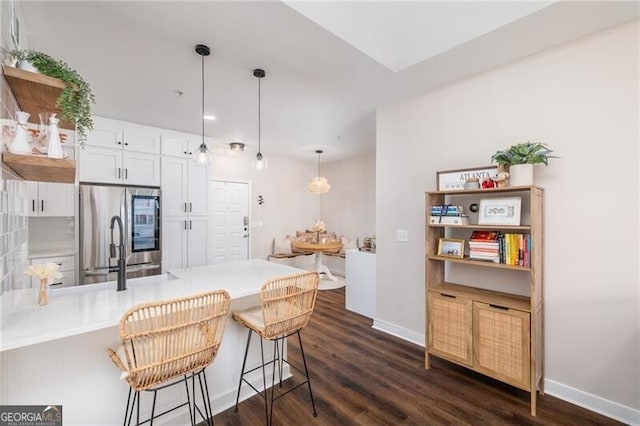 kitchen featuring pendant lighting, stainless steel refrigerator, white cabinetry, a kitchen breakfast bar, and dark hardwood / wood-style flooring