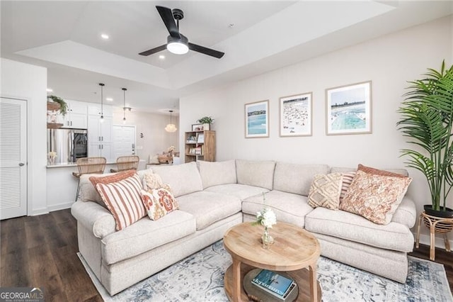 living room featuring a raised ceiling, dark wood-type flooring, and ceiling fan