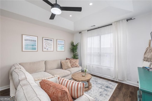 living room featuring dark wood-type flooring, ceiling fan, and a tray ceiling