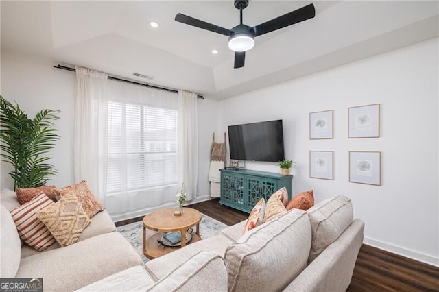 living room with ceiling fan, dark hardwood / wood-style flooring, and a tray ceiling