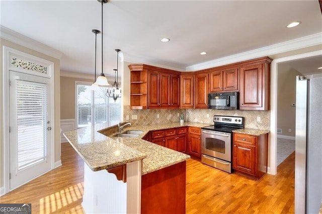 kitchen with a breakfast bar, sink, decorative light fixtures, appliances with stainless steel finishes, and kitchen peninsula