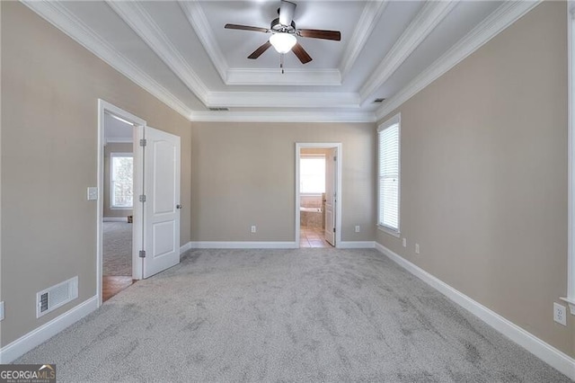 empty room with light carpet, ornamental molding, a raised ceiling, and a healthy amount of sunlight