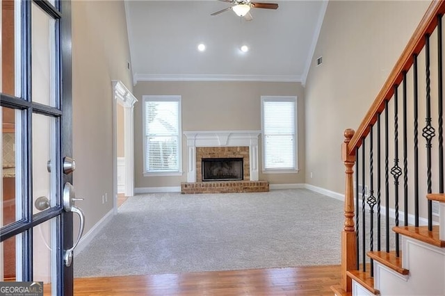 unfurnished living room featuring a brick fireplace, light colored carpet, ornamental molding, and ceiling fan