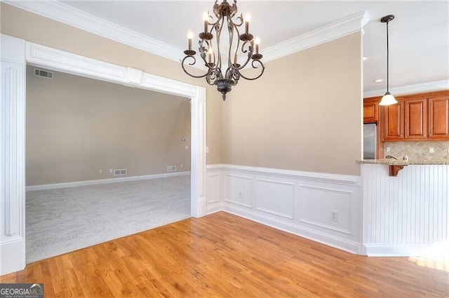 unfurnished dining area featuring an inviting chandelier, ornamental molding, and light wood-type flooring