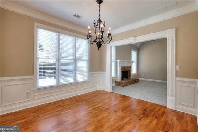 interior space featuring ornamental molding, a brick fireplace, wood-type flooring, and a notable chandelier