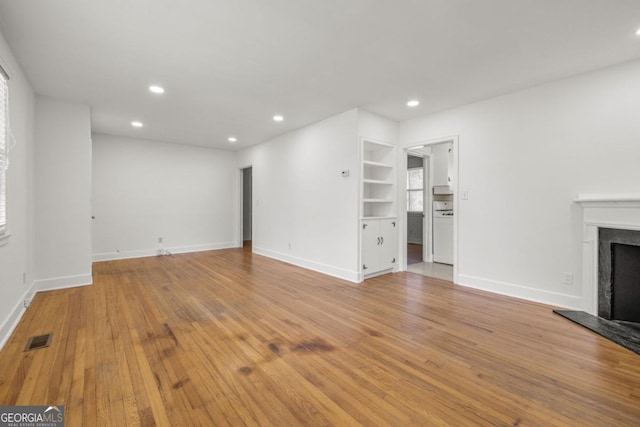 unfurnished living room with built in features and light wood-type flooring