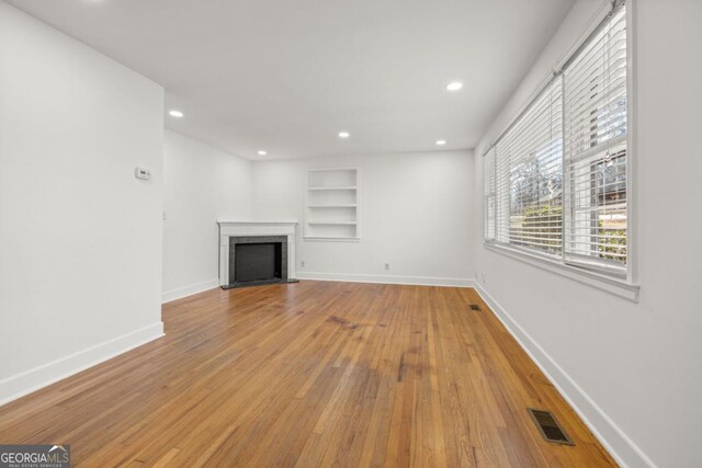 unfurnished living room featuring built in features and light wood-type flooring